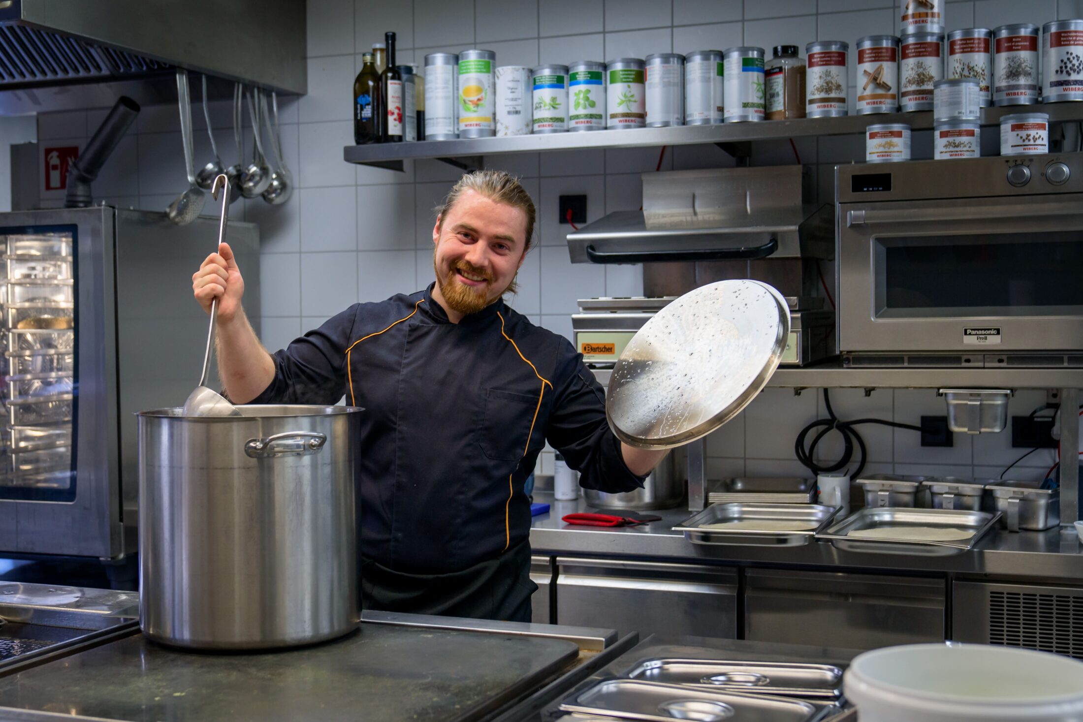 Unser Küchenchef lachend mit Kelle und Topfdeckel in der Küche