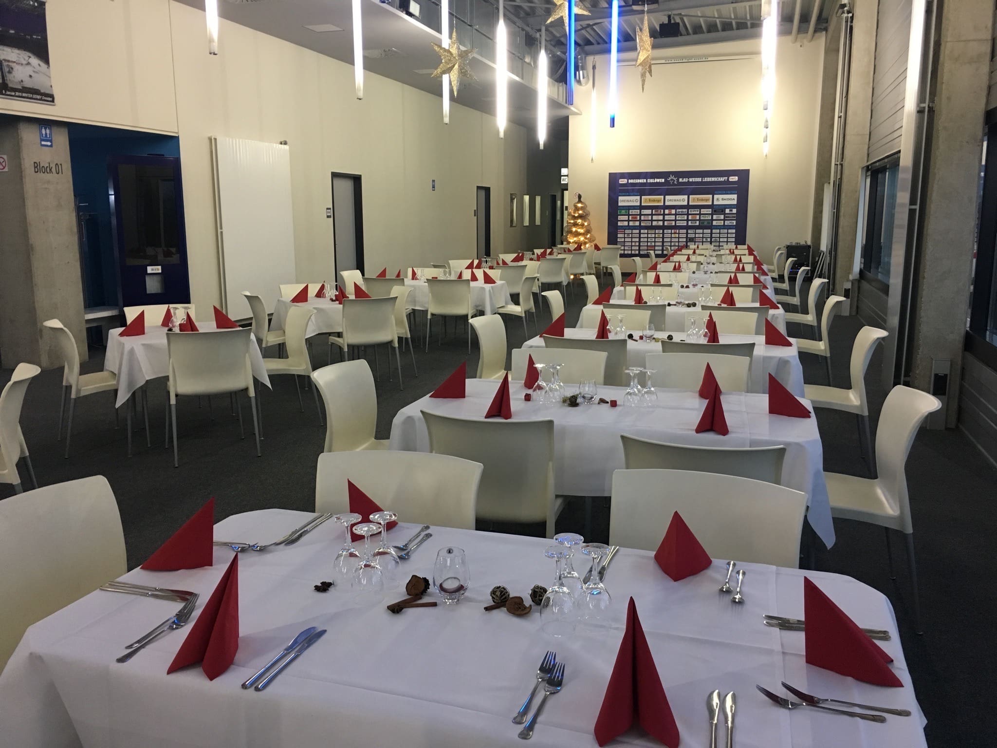 Festlich eingedeckter Saal mit weißen Stühlen und langen Tafeln